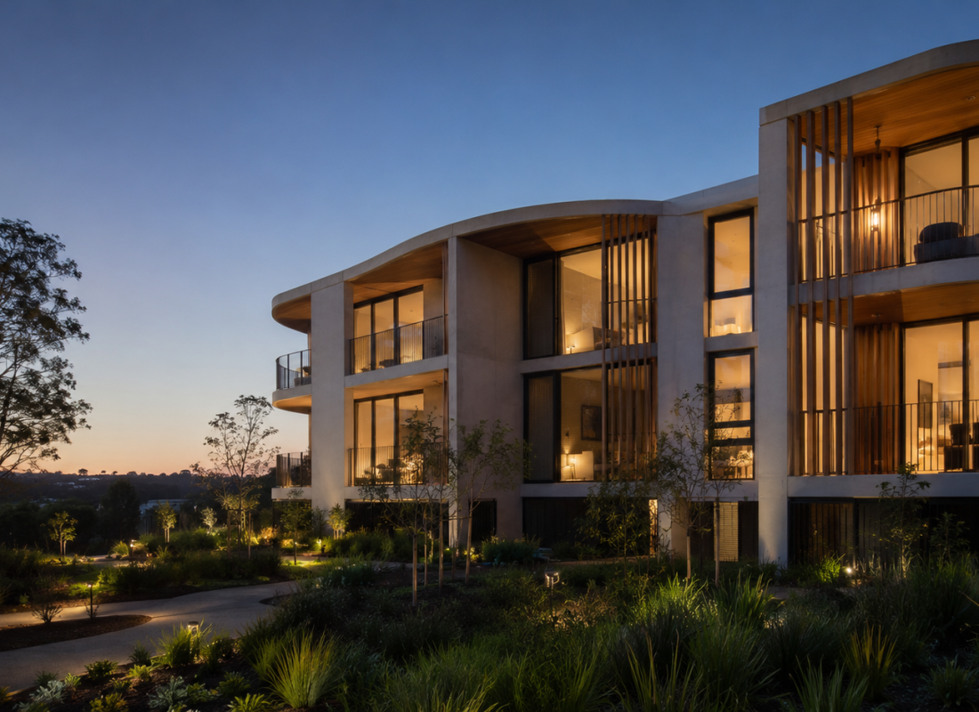 Contemporary low-rise apartment development at blue-hour dusk, warm-lit windows and native garden