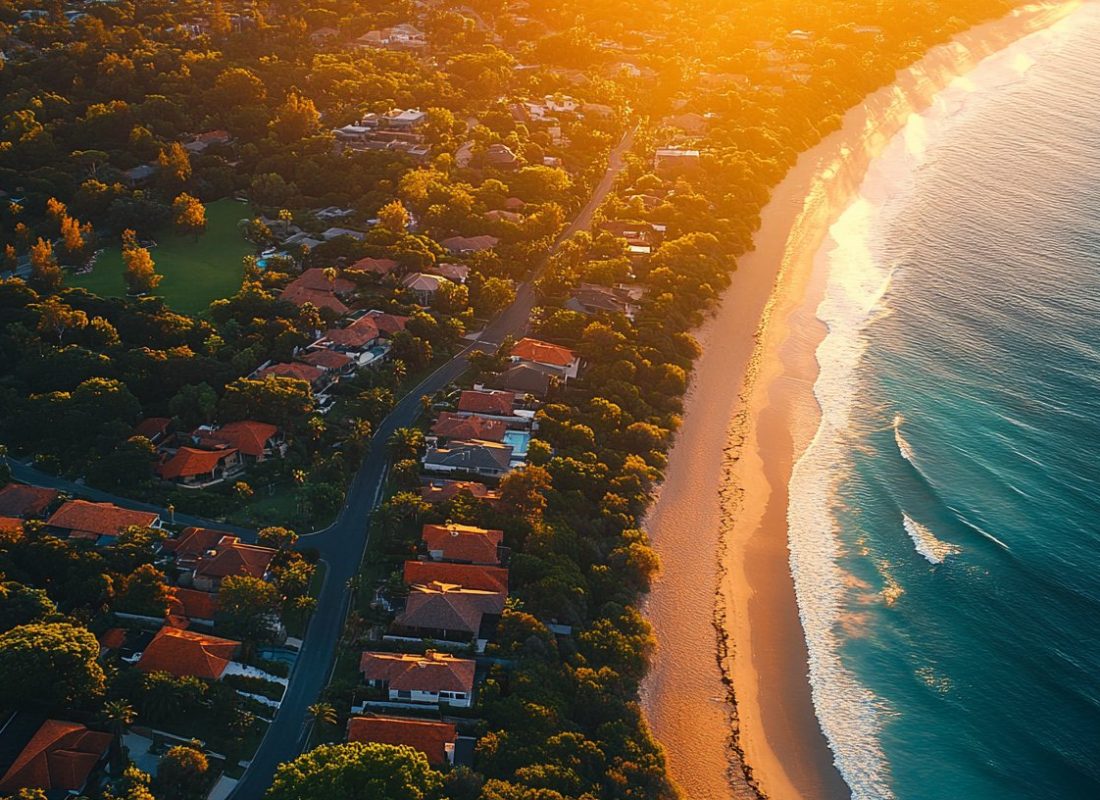Aerial view of an Australian coastal suburb at golden hour, rooftops sweeping down to the beach