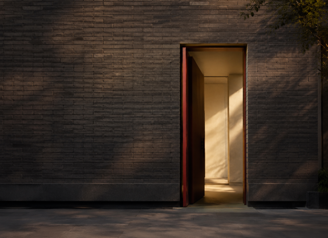 Contemporary charcoal brick wall with one open doorway framed in deep red, warm light passing through